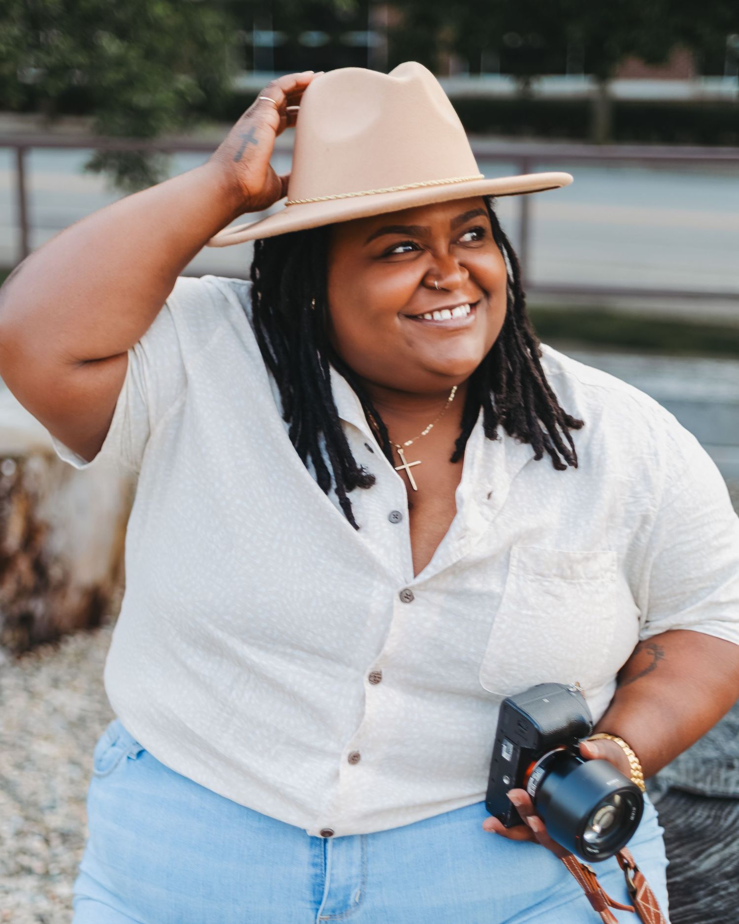 Photographer in white shirt and beige hat poses with camera outdoors.