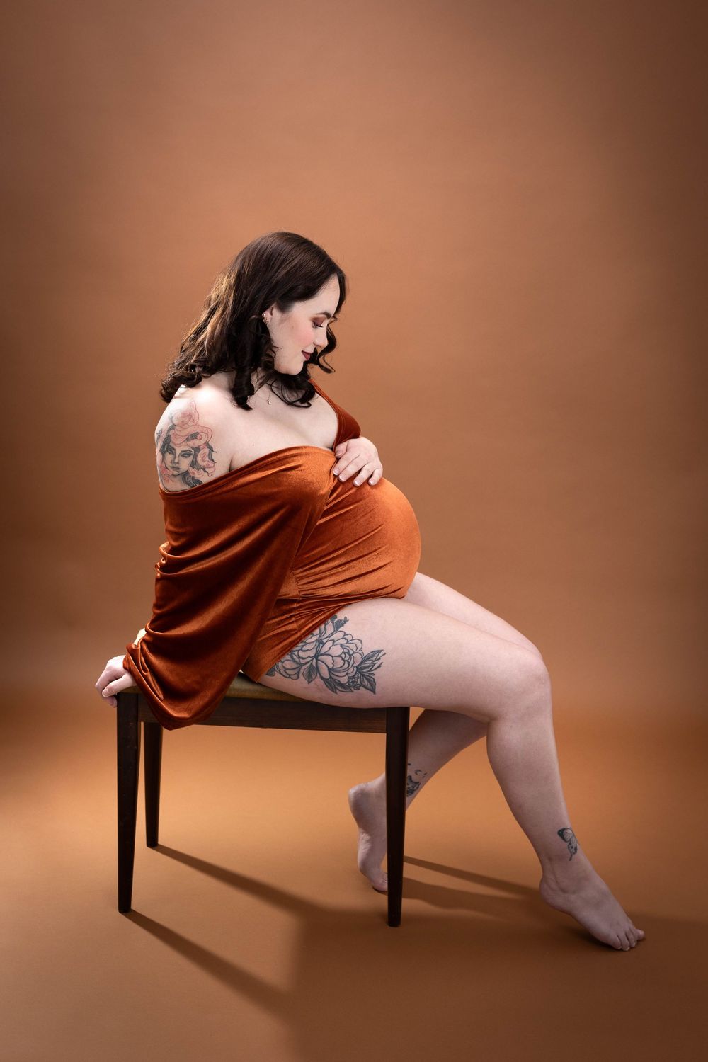 A figure in a rust-colored dress poses artistically on a wooden chair against a brown backdrop in a photo series.