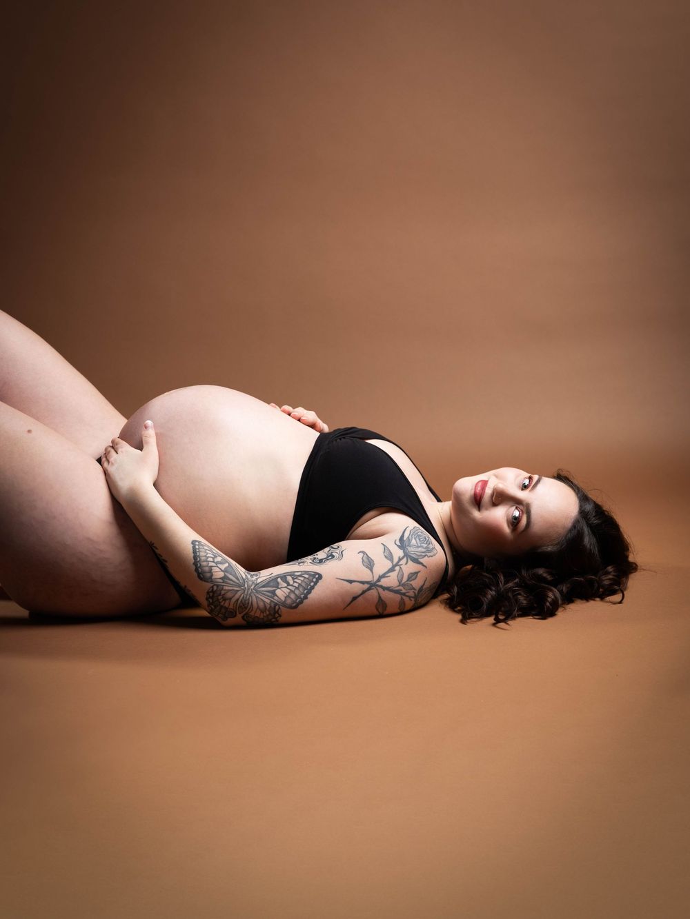 A series of artistic maternity photos showing a pregnant woman in black lingerie reclining against a brown backdrop.