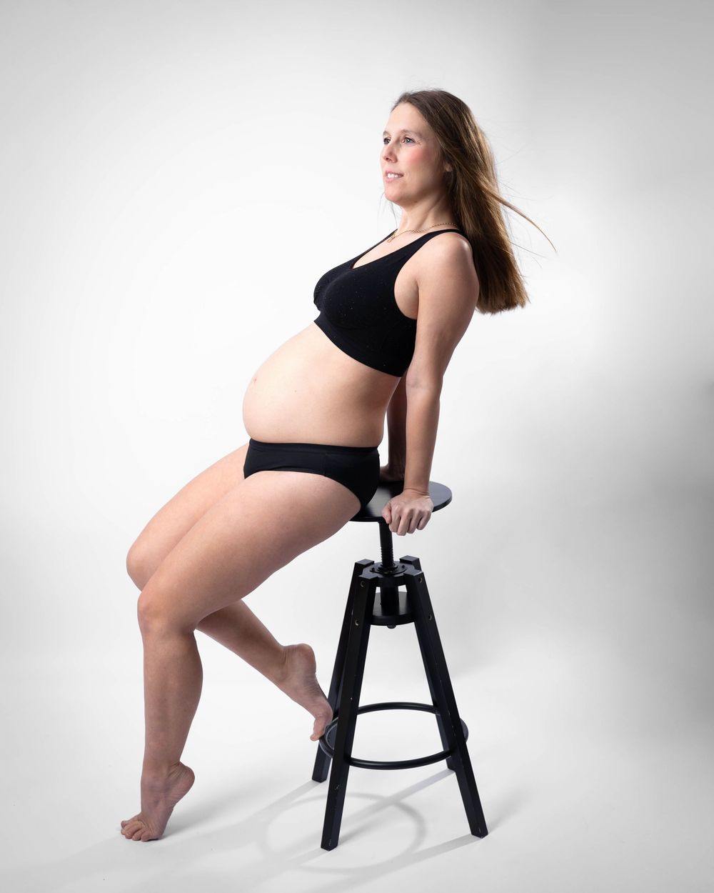 A figure in black athletic wear poses artistically on a black stool against a white studio backdrop in four different poses.