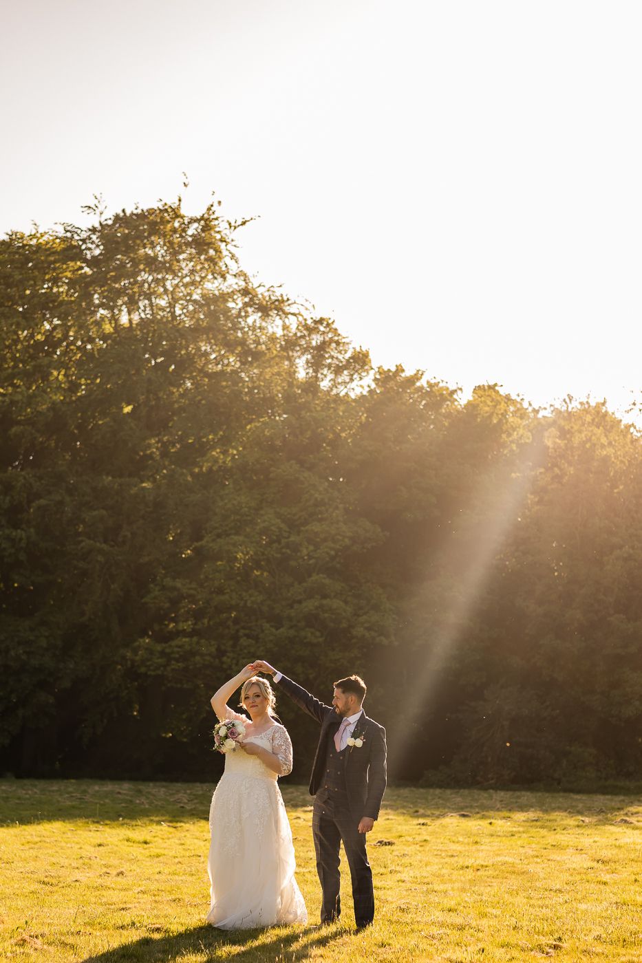 Newlyweds share a romantic moment in a sunlit meadow during golden hour.