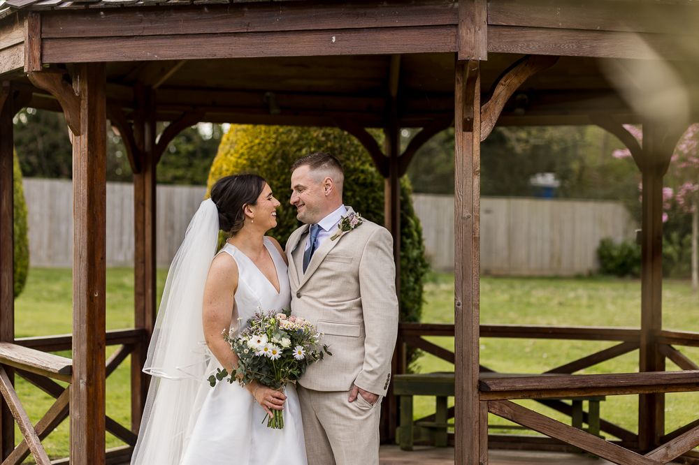 A couple shares an intimate moment under a rustic wooden pergola during their outdoor wedding celebration.