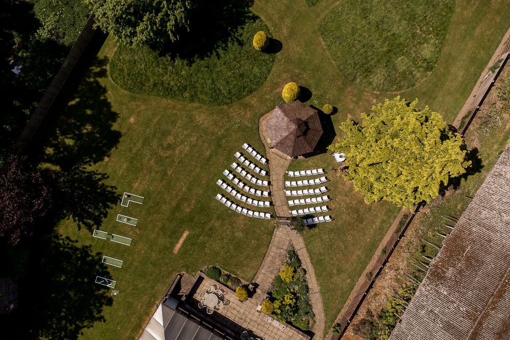 Aerial view of a wedding venue surrounded by lush green lawns and gardens on a sunny day.