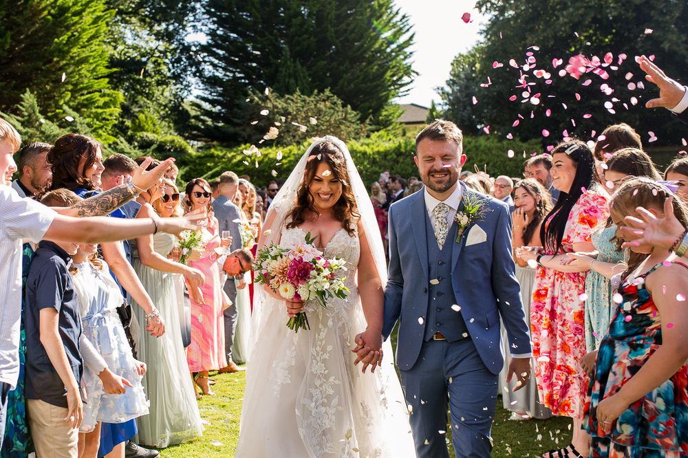 Wedding guests celebrate and throw confetti at an outdoor ceremony.