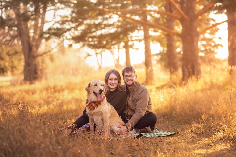 Couple and their dog enjoy a golden sunset in a forest setting during an outdoor photo session.