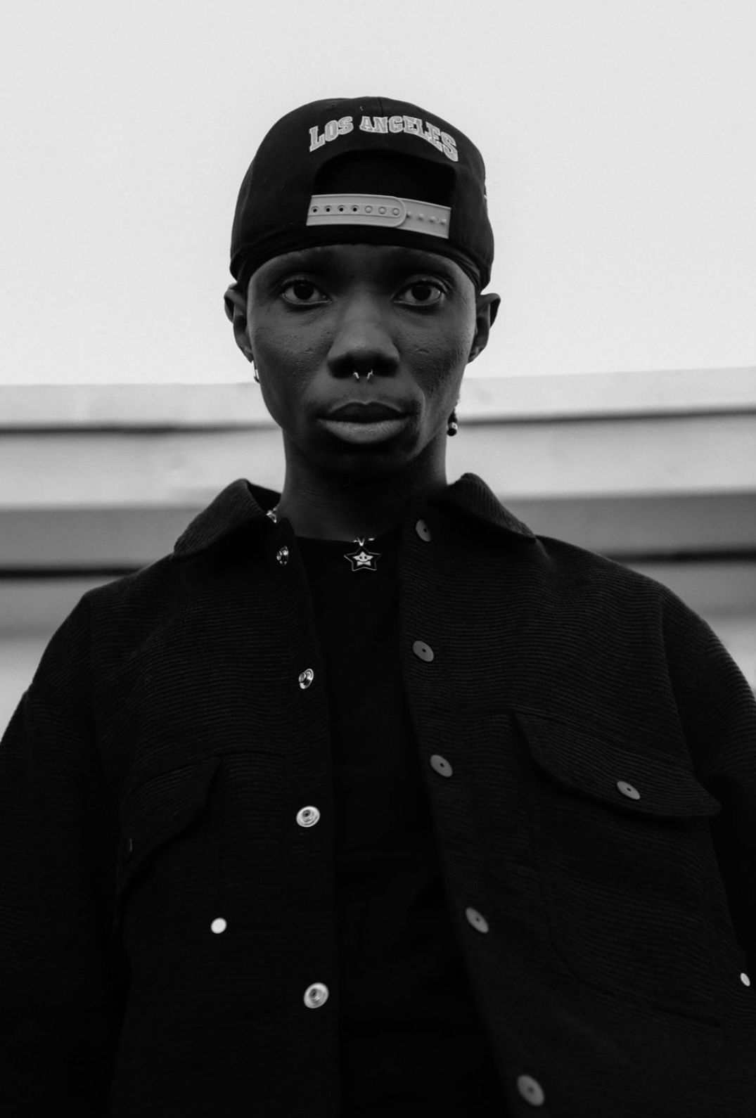 Black and white portrait of someone wearing a dark jacket and baseball cap against a light background.