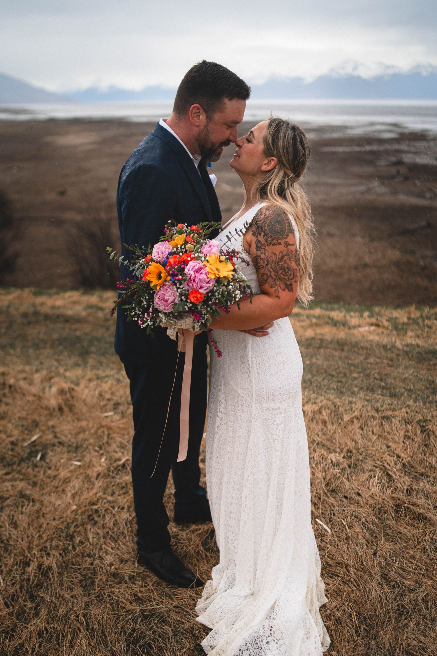 Bride holding a colorful wedding bouquet of blue, burgundy, and white roses with a diamond engagement ring.