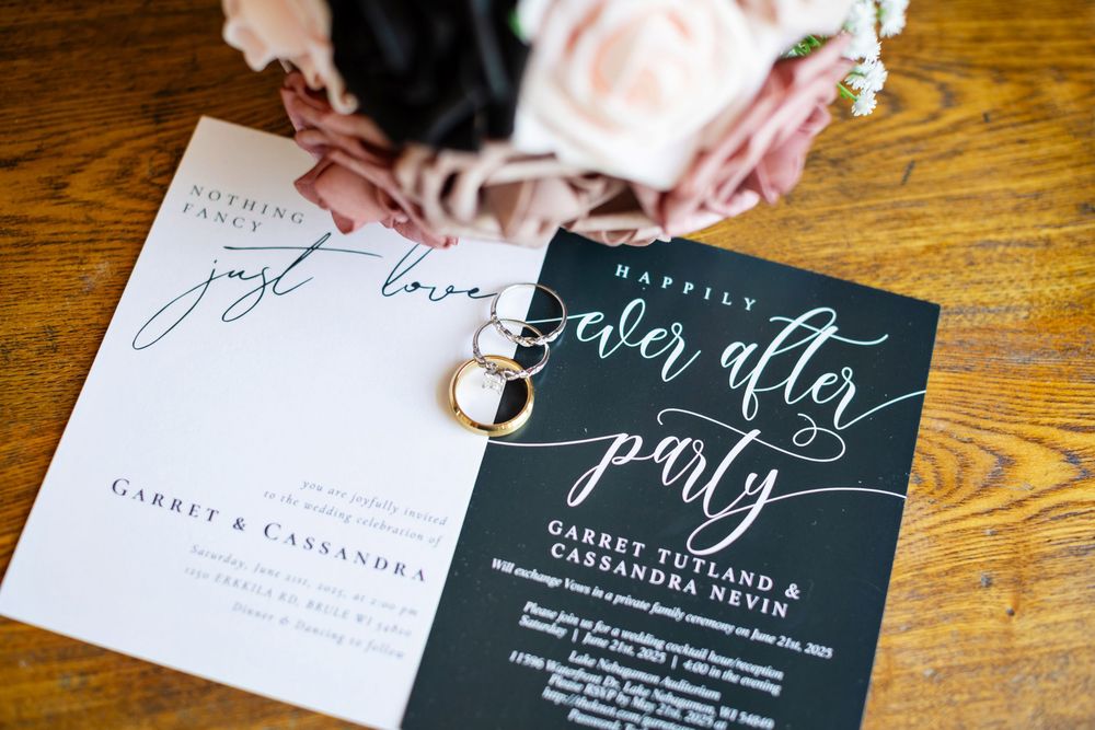 Wedding invitation calligraphy details being written on dark envelopes with white ink on a wooden table surface.