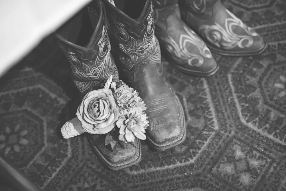 Black and white photo showing feet in boots dancing on a patterned rug at a wedding celebration.