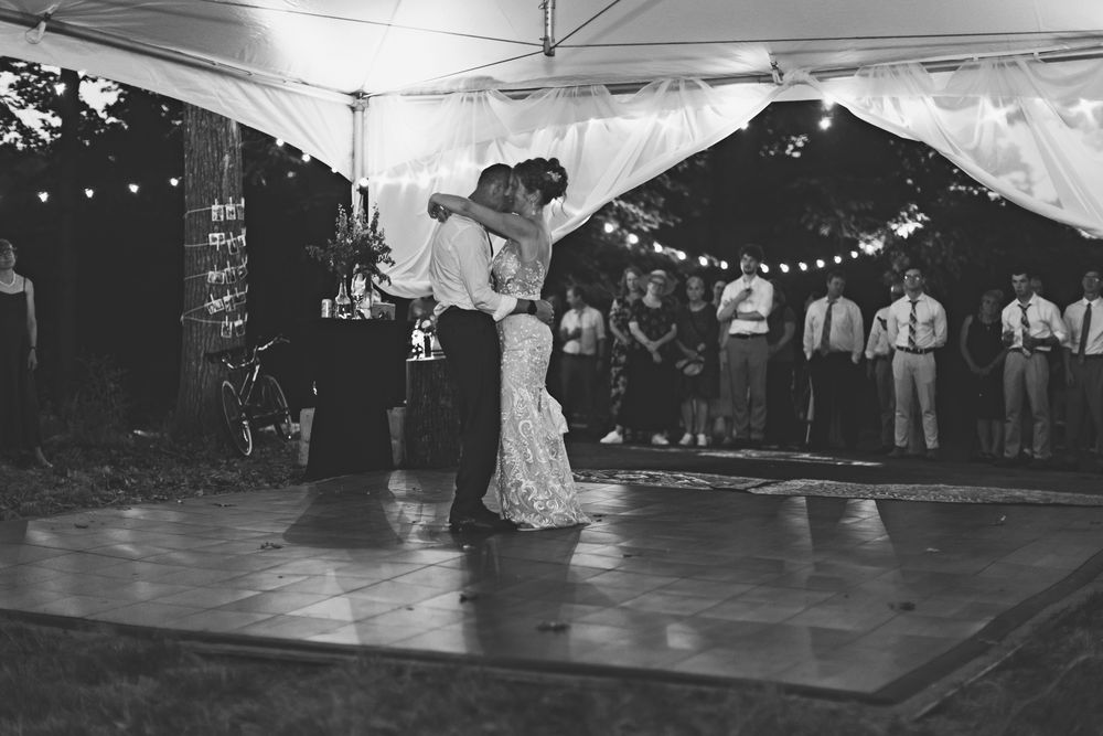 A black and white photo shows couples dancing together on a wooden dance floor under string lights.
