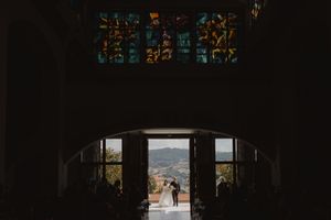 Gli sposi in silhouette nel portone di una chiesa, con le colline sullo sfondo.