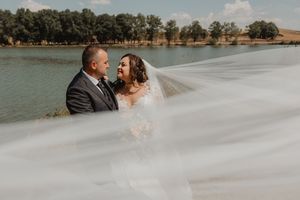 Gli sposi si abbracciano accanto al lago, con il velo della sposa in primo piano.