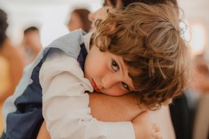 Un bambino con i capelli ricci appoggia la testa a una spalla durante il matrimonio.