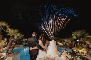 Gli sposi si abbracciano accanto alla torta e alla piscina mentre i fuochi illuminano il cielo.