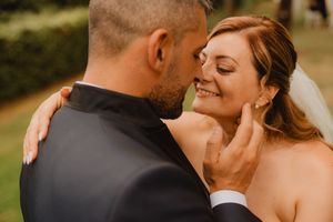 Lo sposo accarezza il viso della sposa sorridente durante i ritratti all’aperto.