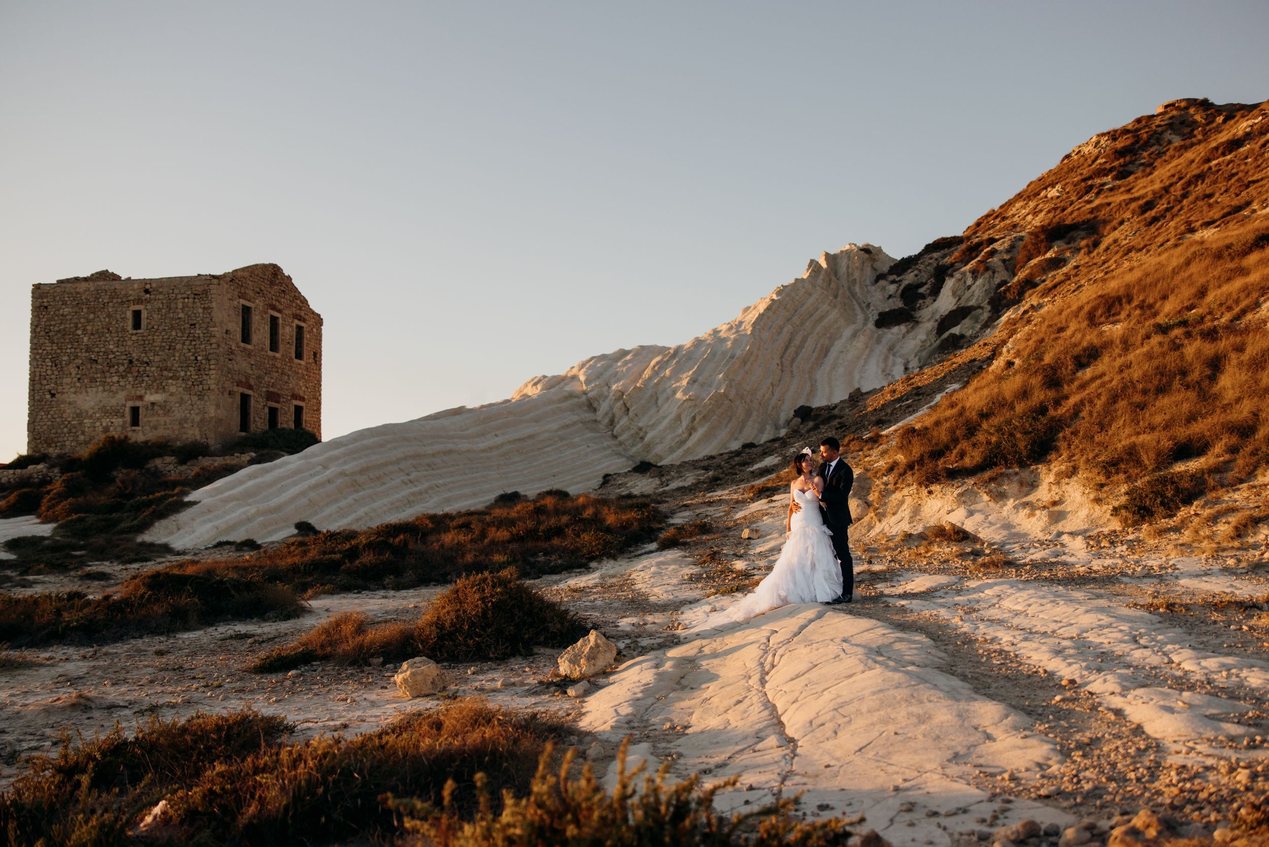 Giovanni e Cristina si baciano vicino a una torre sulle scogliere siciliane.