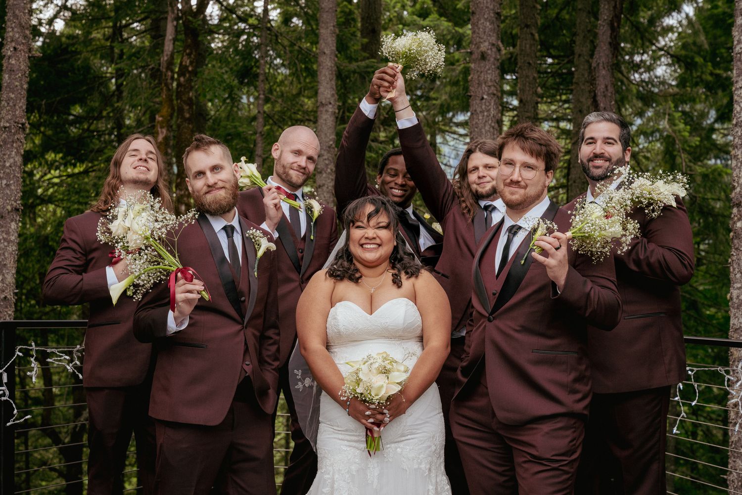 Mixed wedding party cheers with bride and groom in Washington forest.