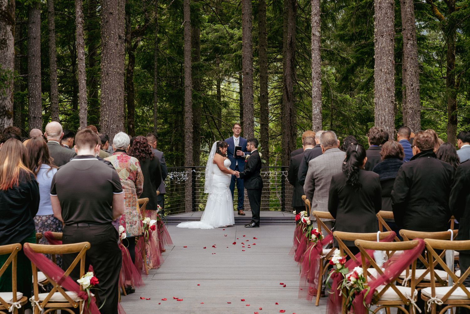 Beautiful outdoor wedding ceremony in Washington State woods, featuring a mixed-race couple and family at a scenic woodland venue.