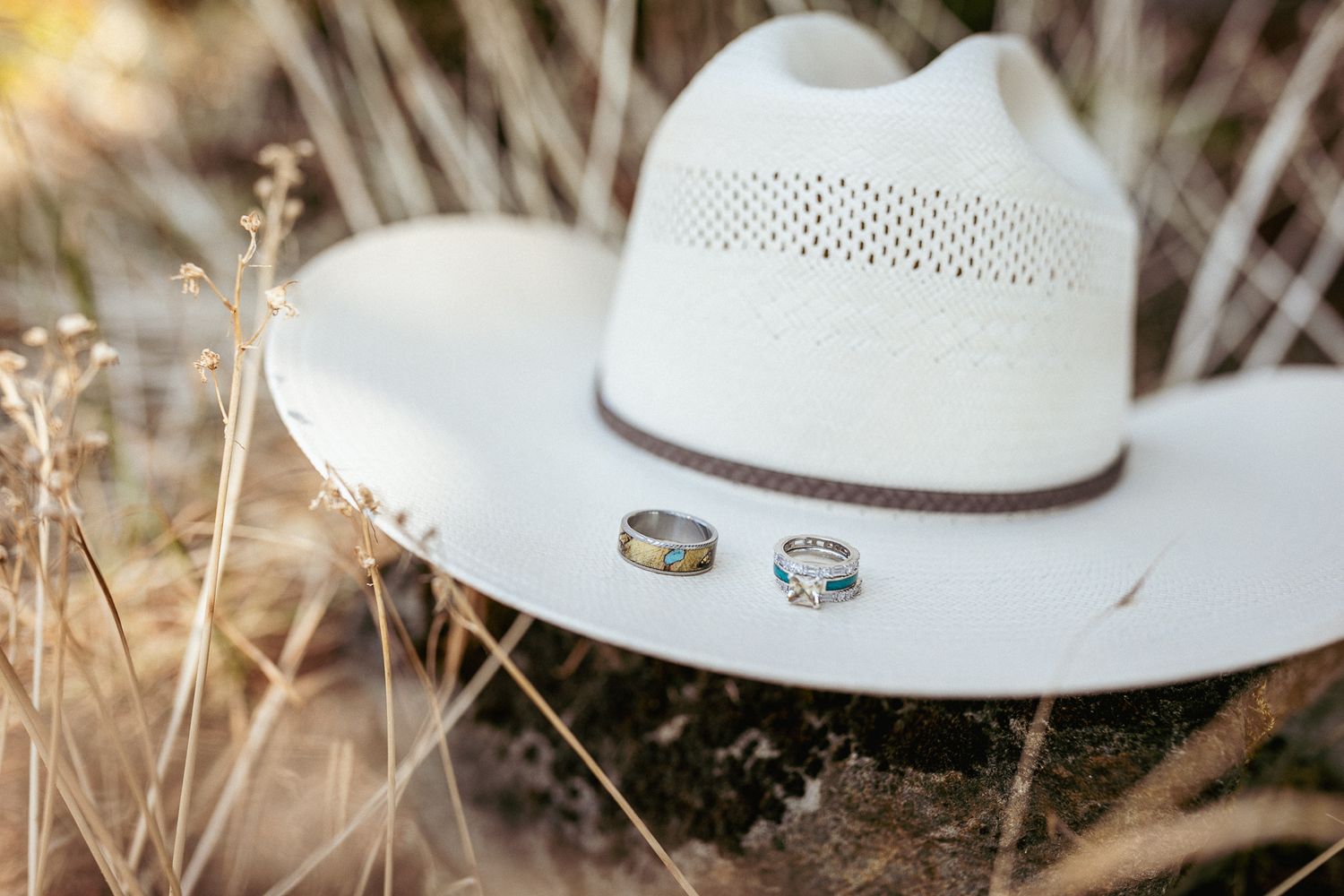 Western-inspired wedding detail shot of rings on a white cowboy hat in a dry grass field, perfect for country weddings.