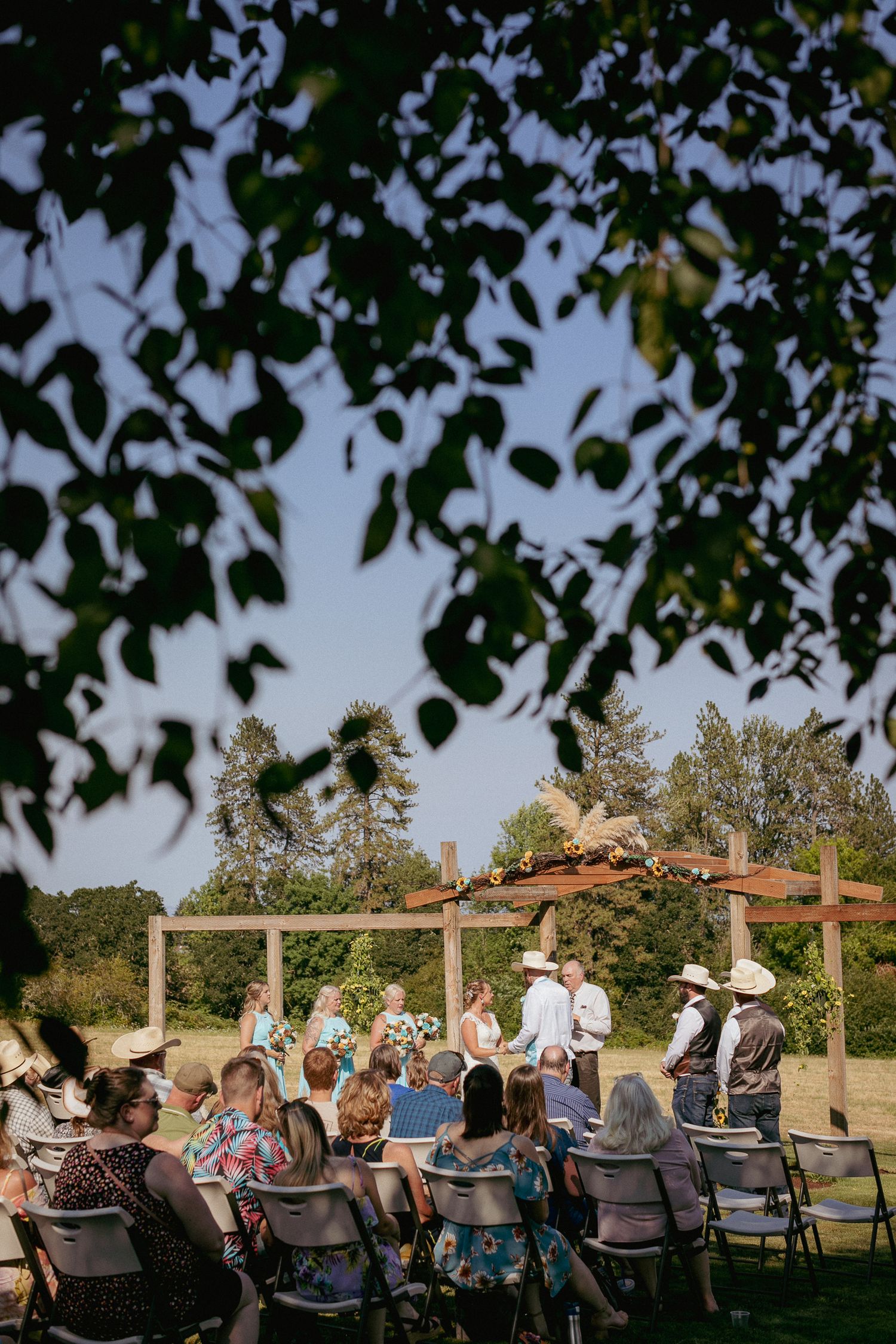 Looking through tree branches at a beautiful outdoor wedding ceremony setup. Natural framing adds depth to scenic venue view.