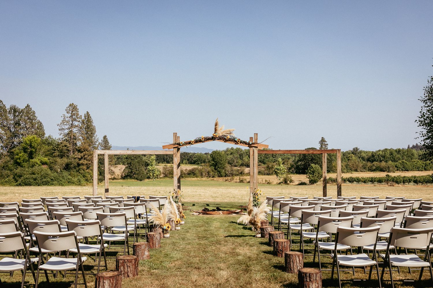 Outdoor ceremony setup with wood arch and rows of chairs on green lawn.
