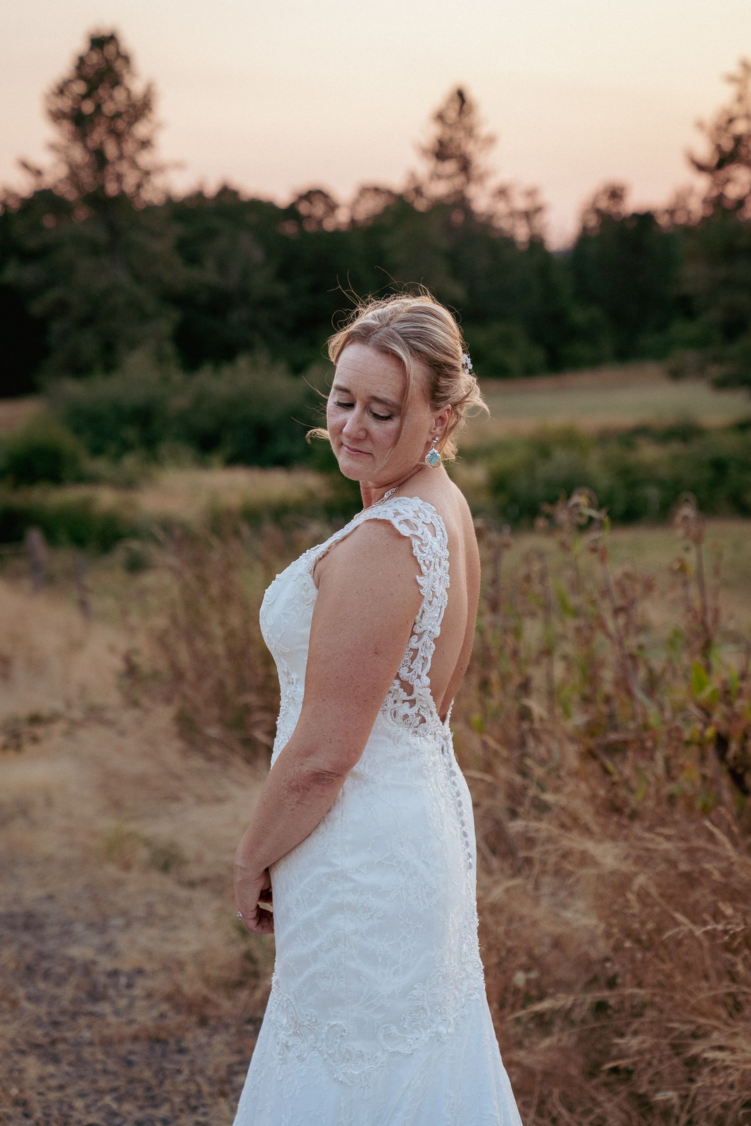 Bride in lace dress stands in golden field, elegant Oregon elopement