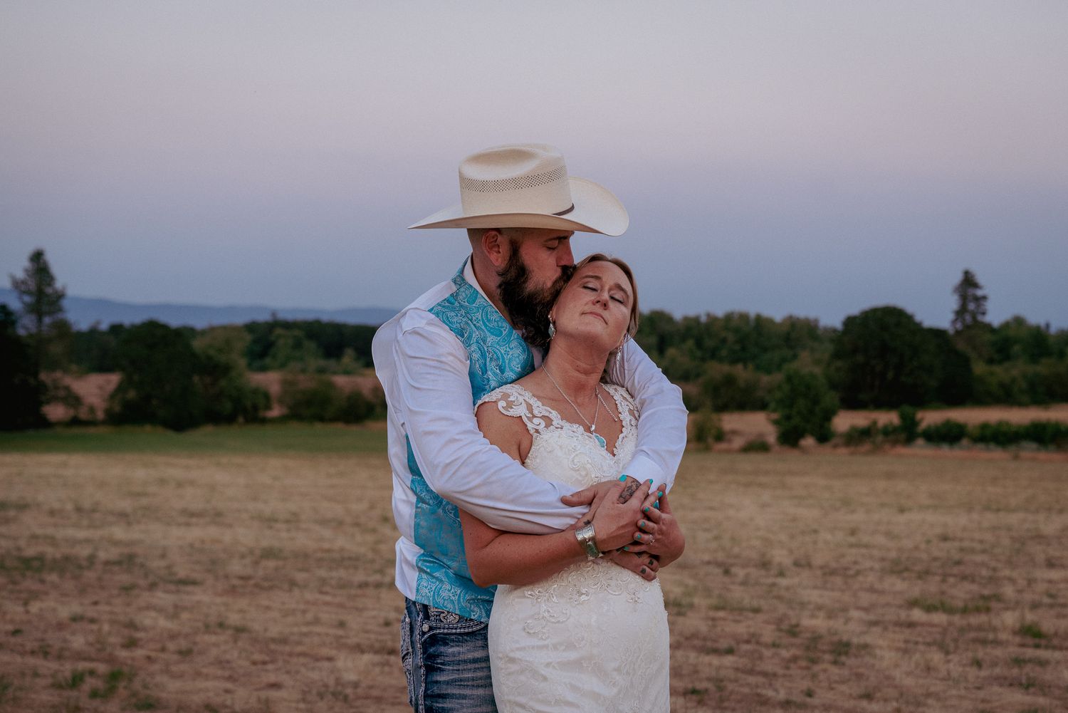 Country couple embraces at sunset in Central Oregon ranch wedding.