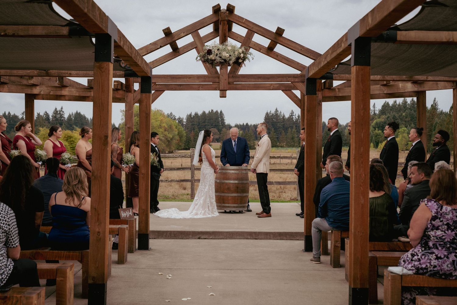 Rustic outdoor wedding ceremony under a wooden arbor with a couple saying vows in front of guests in the Willamette Valley