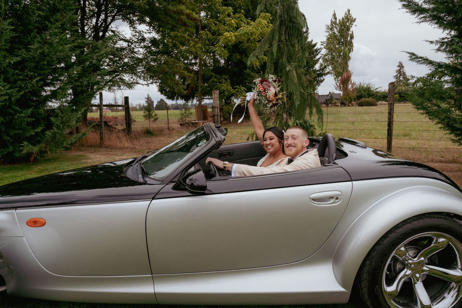 Newlywed couple celebrates in a convertible getaway car, holding the bouquet high after a joyful Washington wedding.