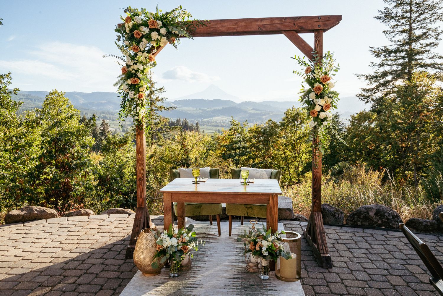 Outdoor wedding sweetheart table for bride and bride, with floral arch and scenic Mt Hood backdrop.