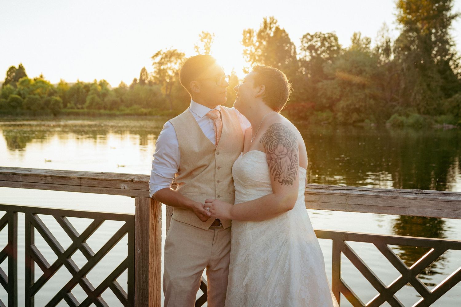 Bride and Groom sharing a kiss at sunset near a lake, surrounded by warm light and lush trees in the background.