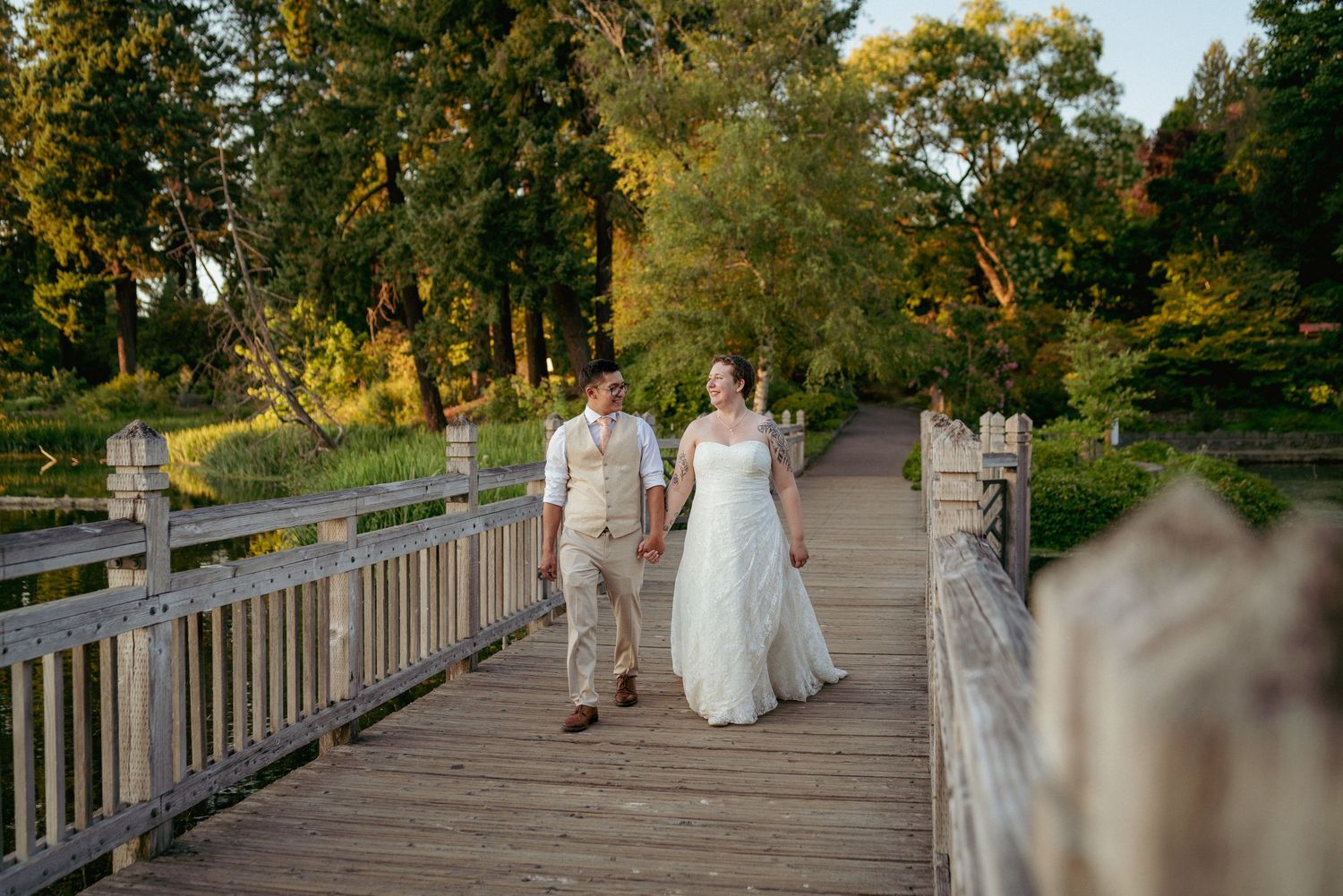 Bride and groom walk hand-in-hand on a rustic PNW bridge.
