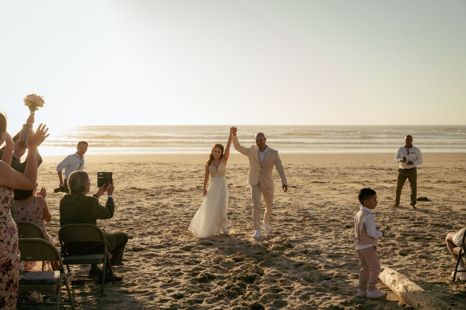 Sunset Oregon beach wedding ceremony, bride and groom walking back to guests after saying their I dos. Romantic coastal celebration moment.