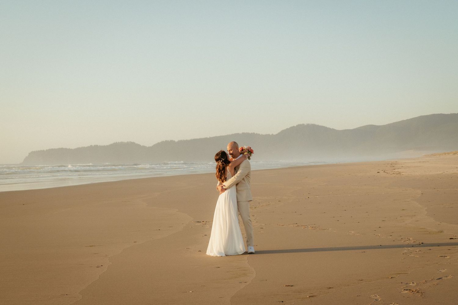 Interracial couple kisses on wide Oregon Coast beach at sunset.