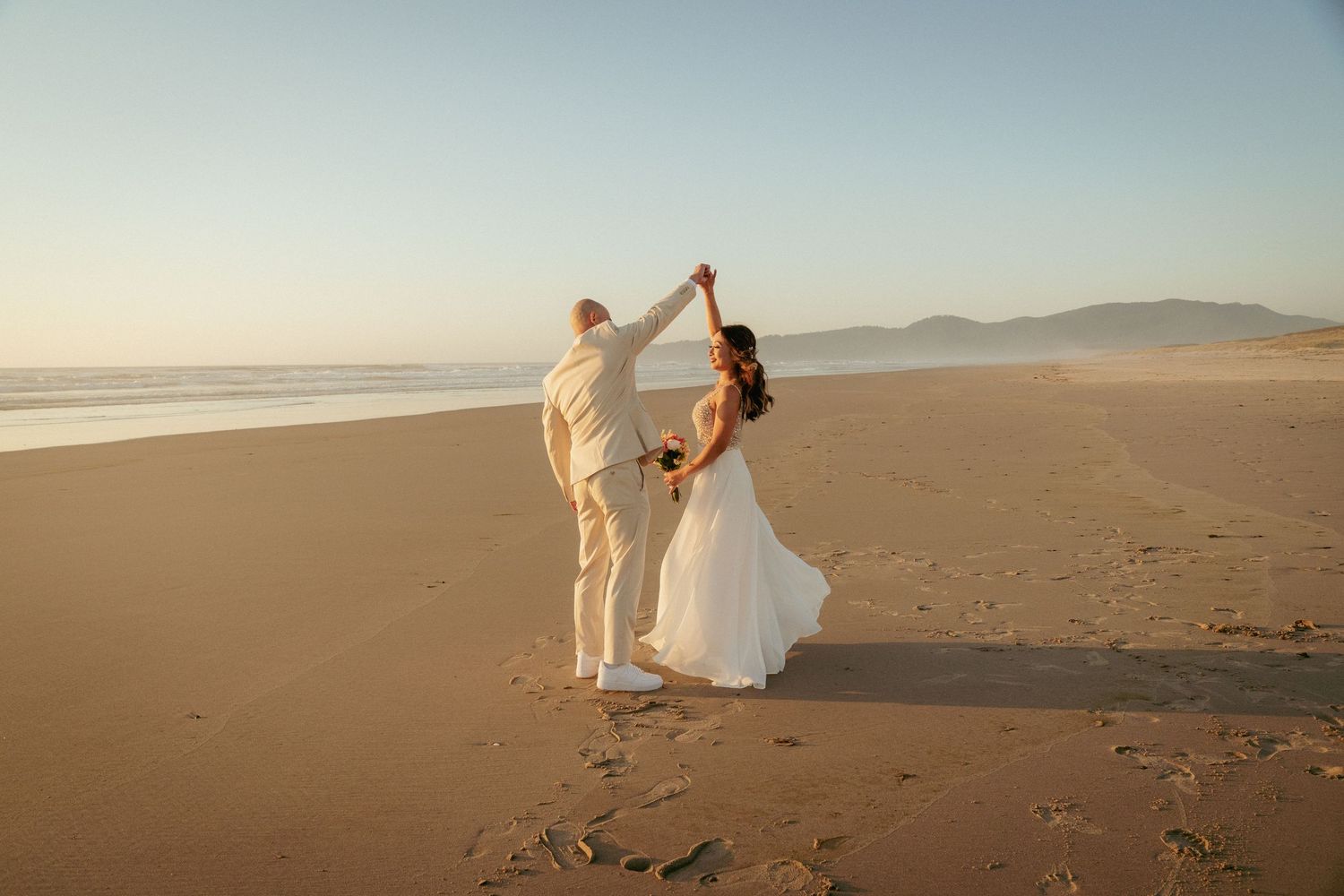 Bride and groom dancing on the Oregon Coast at sunset, capturing a romantic beach wedding moment.