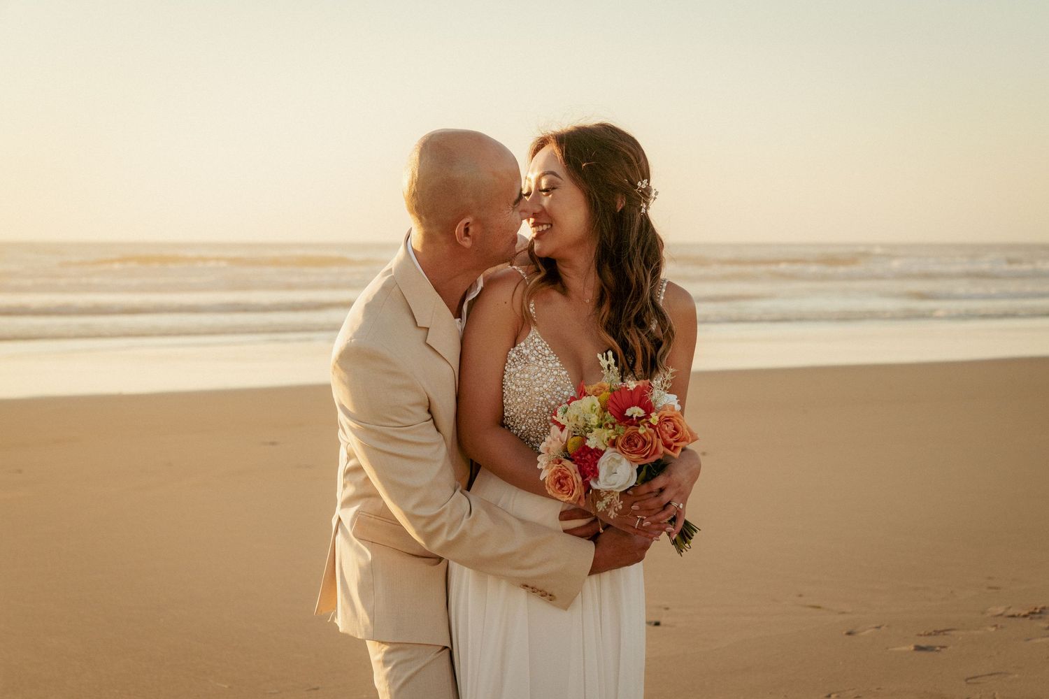 Interracial couple kisses on beach at sunset, joyful Oregon elopement.