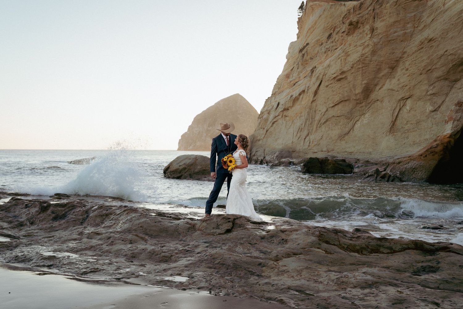 Couple kisses on rocks as waves crash at Cape Kiwanda, Oregon elopement.