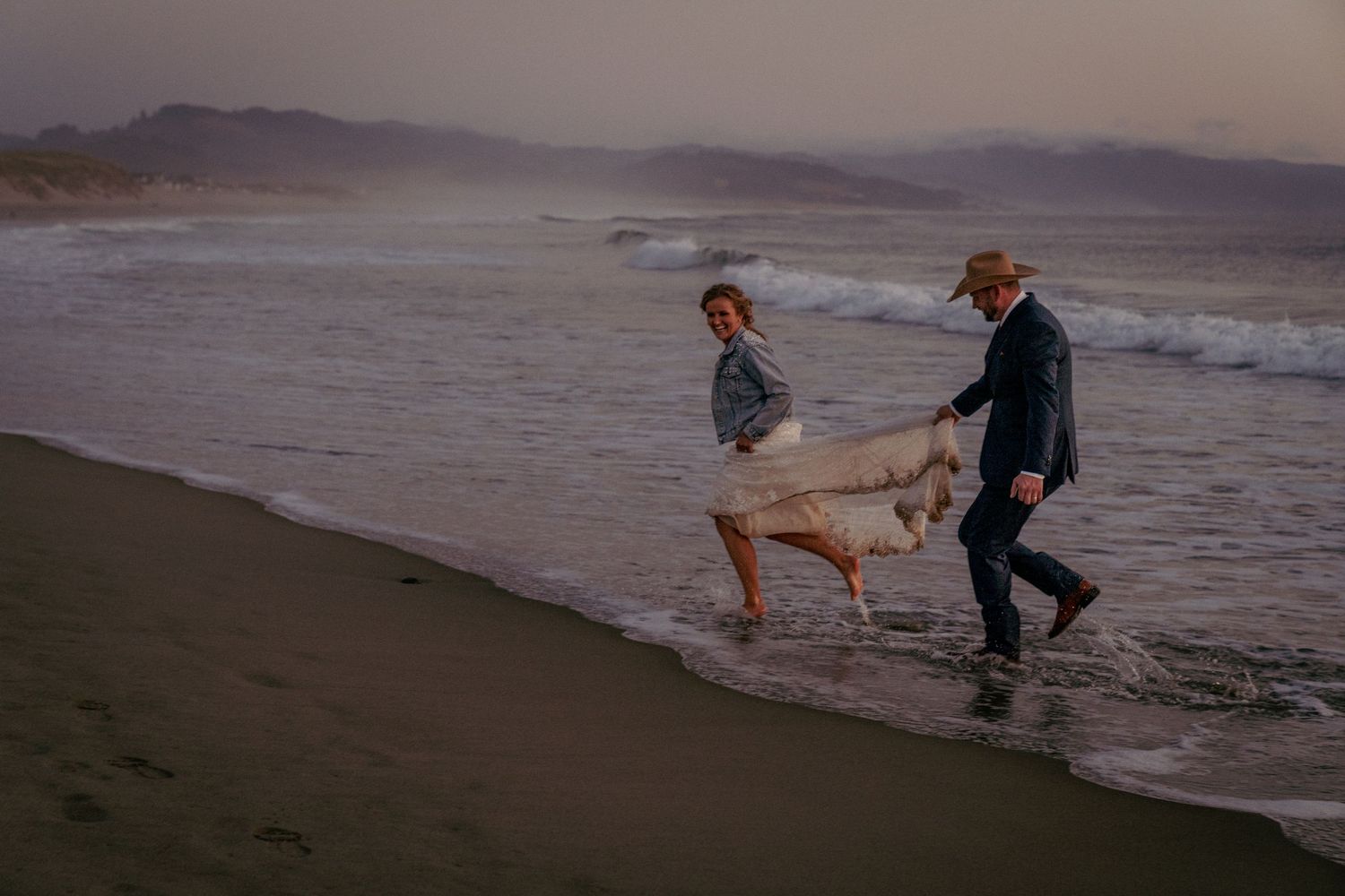 Couple runs barefoot on beach, candid Oregon Coast engagement session.