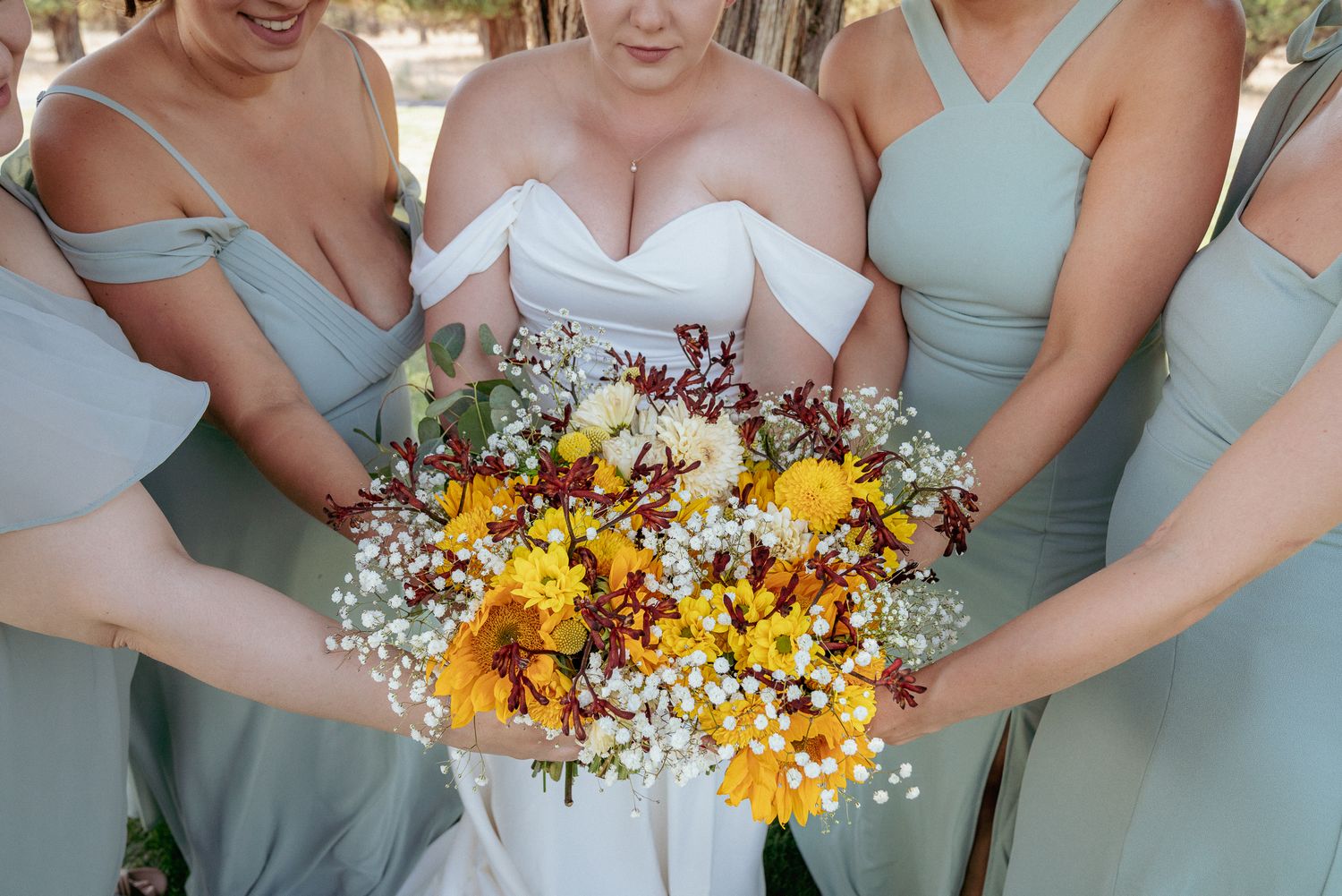 Bride holding wildflower bouquet surrounded by bridesmaids in pastel dresses.
