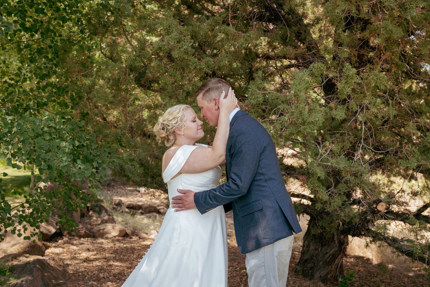 Groom kisses bride’s cheek in forest, romantic Central Oregon moment.