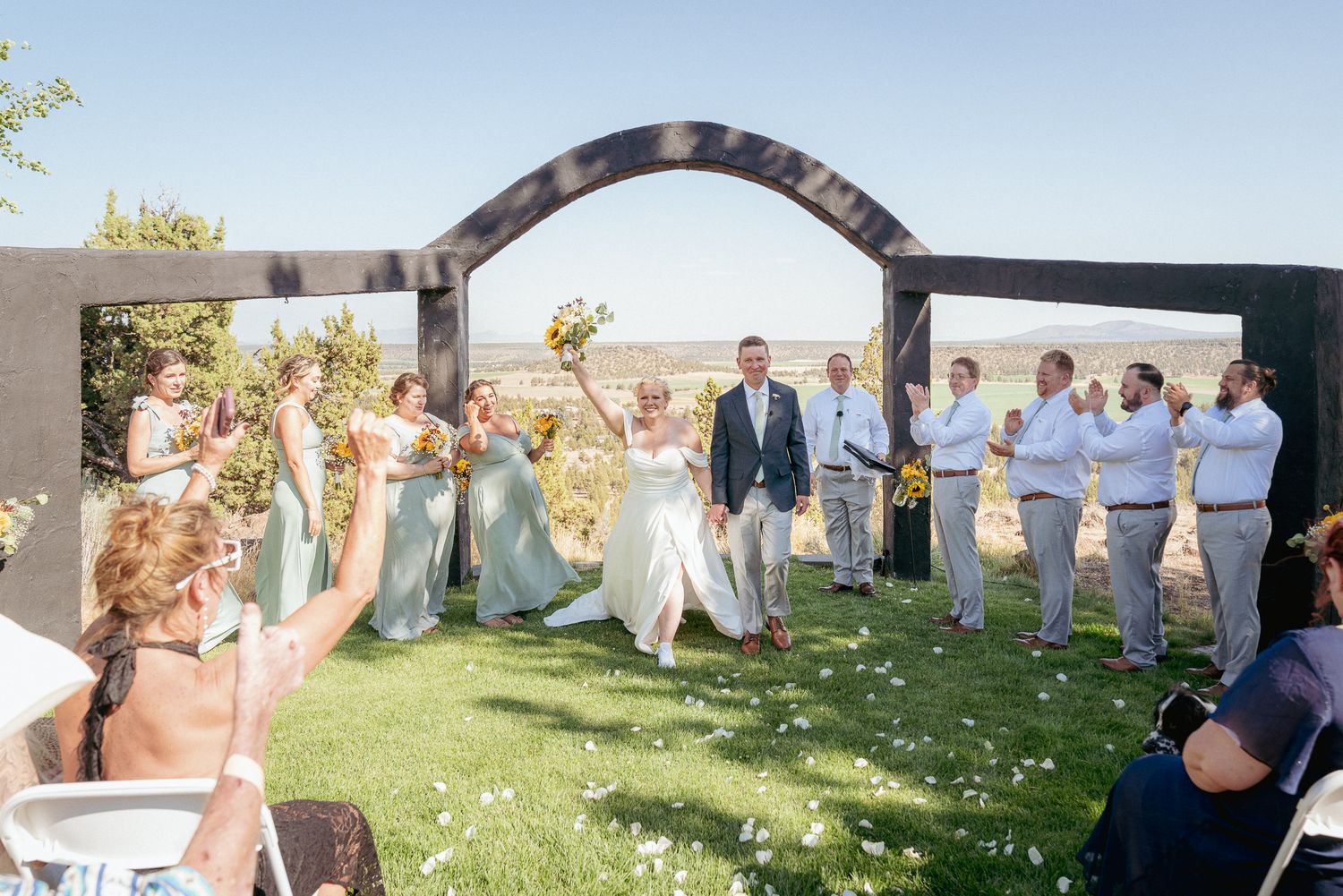 Wedding party cheers during ceremony under arch in Bend Oregon Wedding.