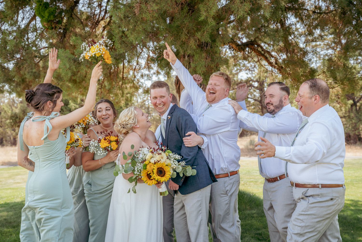 Wedding party cheers with sunflowers in hand, celebrating joyfully in a vibrant backyard wedding setting.