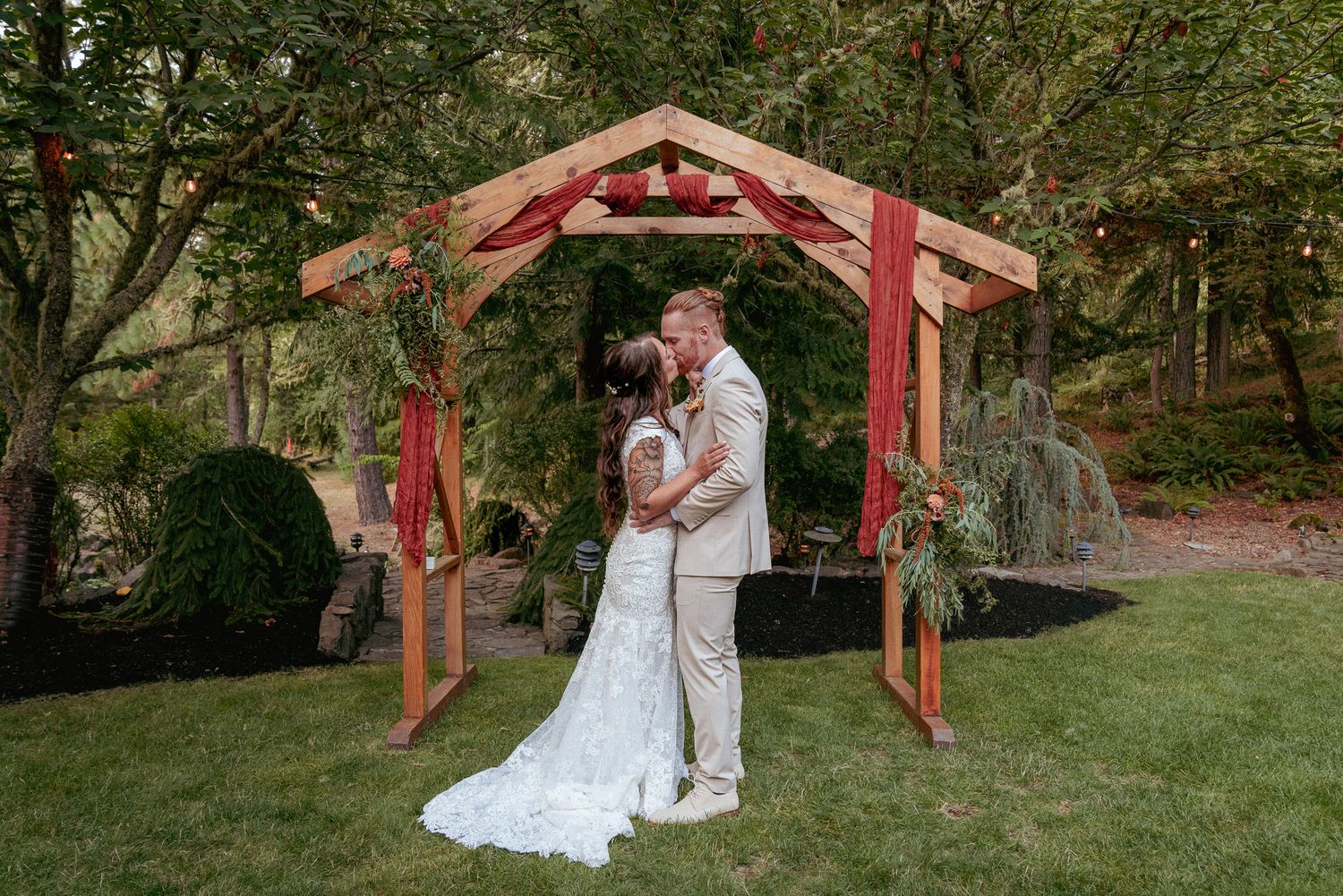 Bride and Groom kiss under cedar arch, backyard Portland wedding.