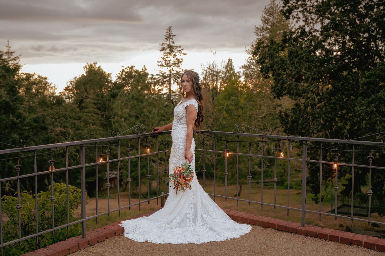Bride holding bouquet, standing on a balcony with forest view. Sunset bridal portrait in Oregon.