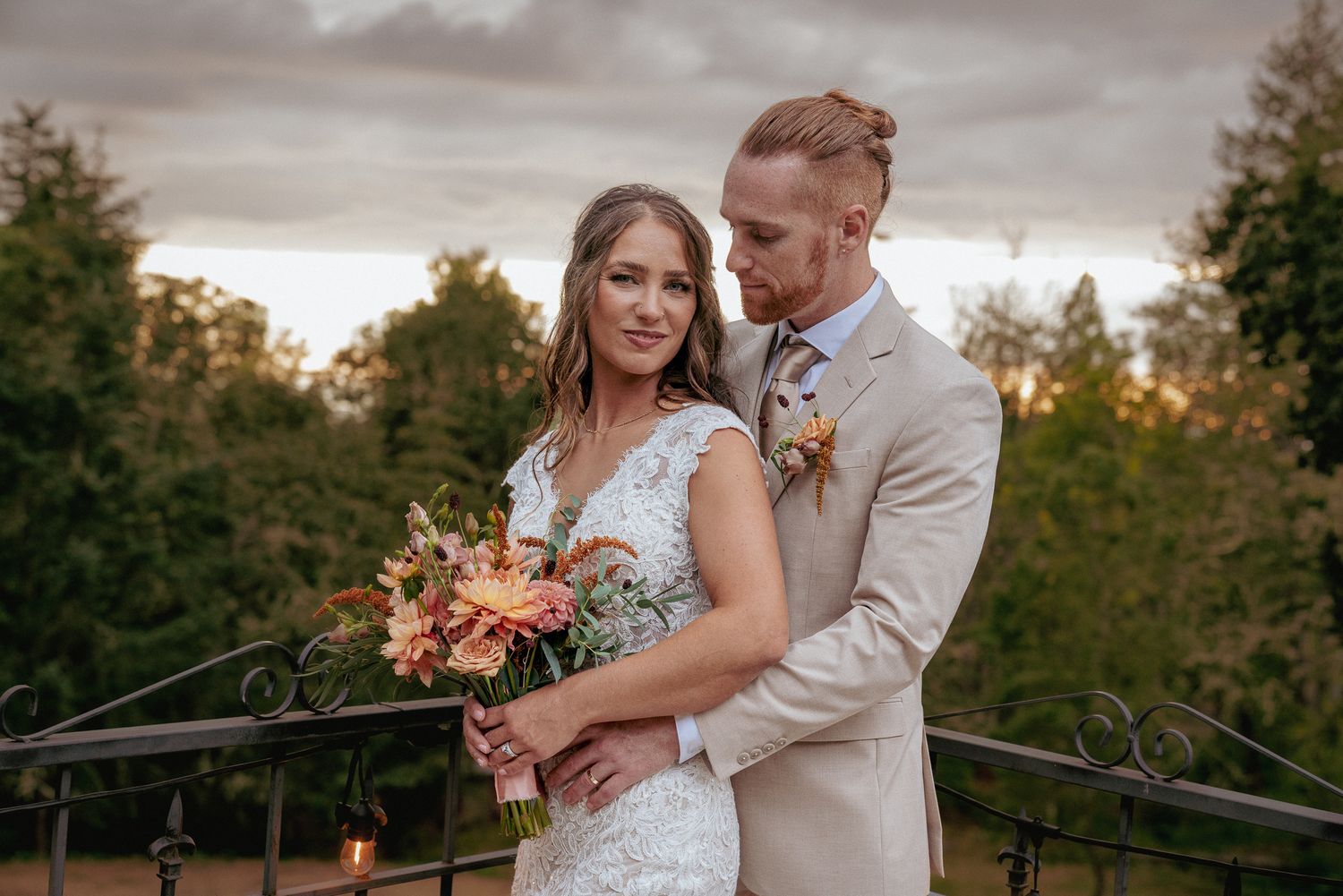 Bride and groom embrace at sunset in outdoor rustic wedding setting.
