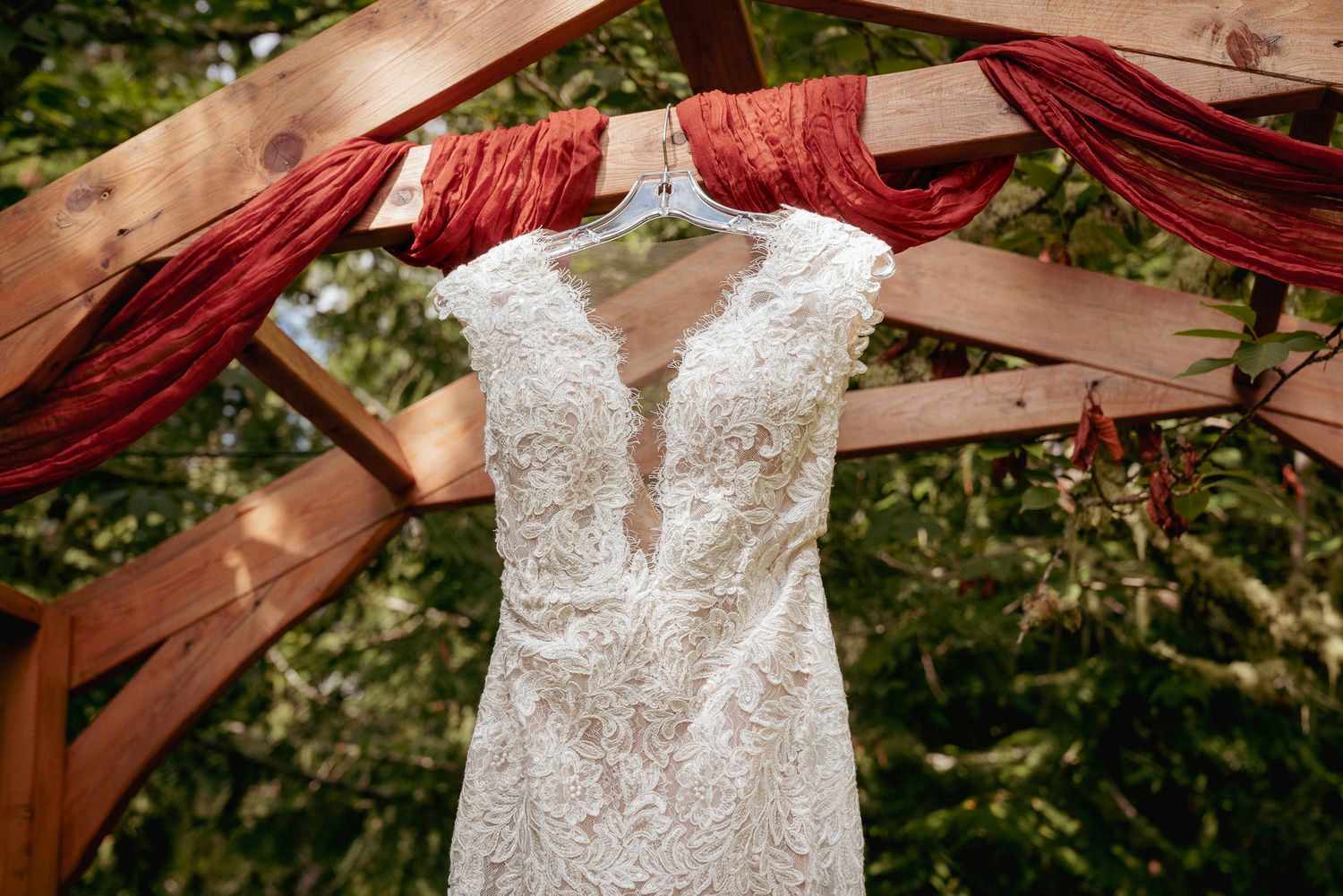 Lace wedding dress hangs on arbor, outdoor ceremony in Portland.