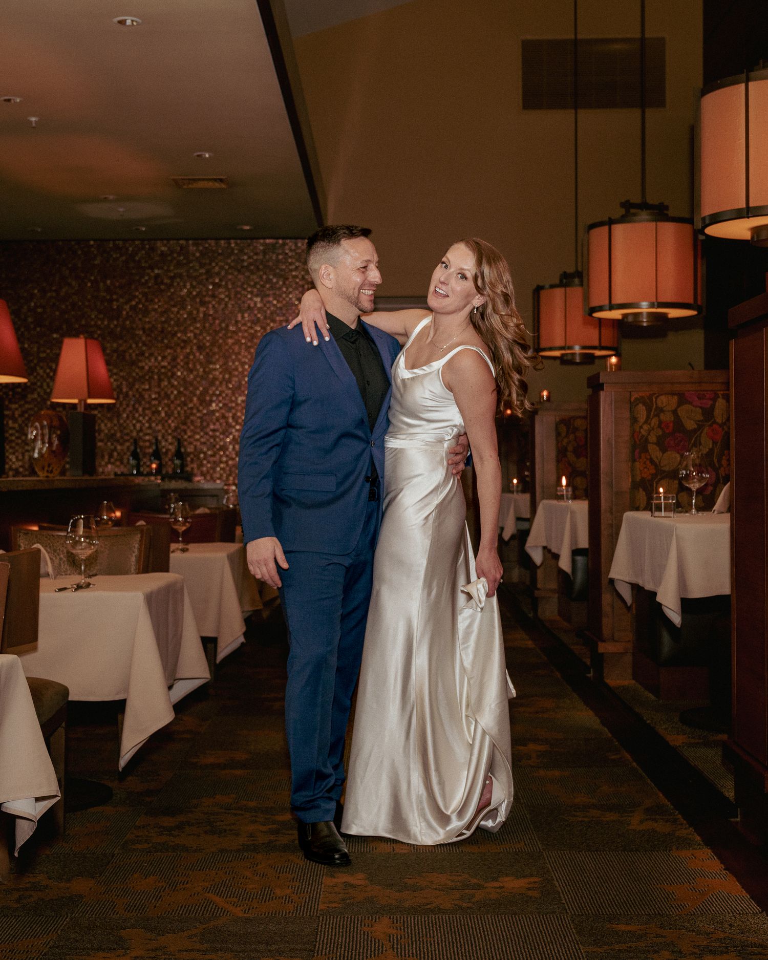 Bride and groom pose inside a cozy restaurant during their small, intimate wedding celebration, dressed in elegant, timeless attire.