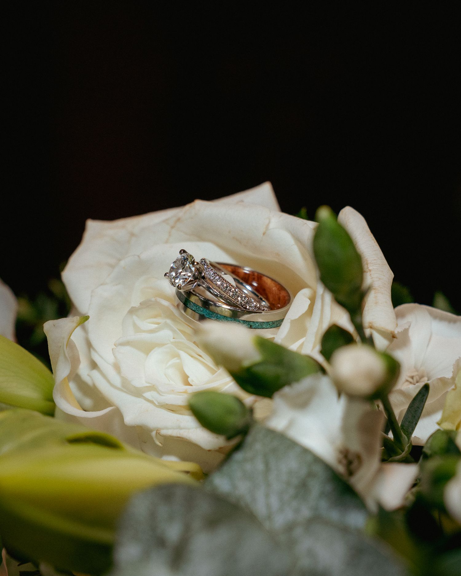 Close-up of wedding rings nestled in a white rose from the bridal bouquet. Elegant floral detail from a romantic wedding.