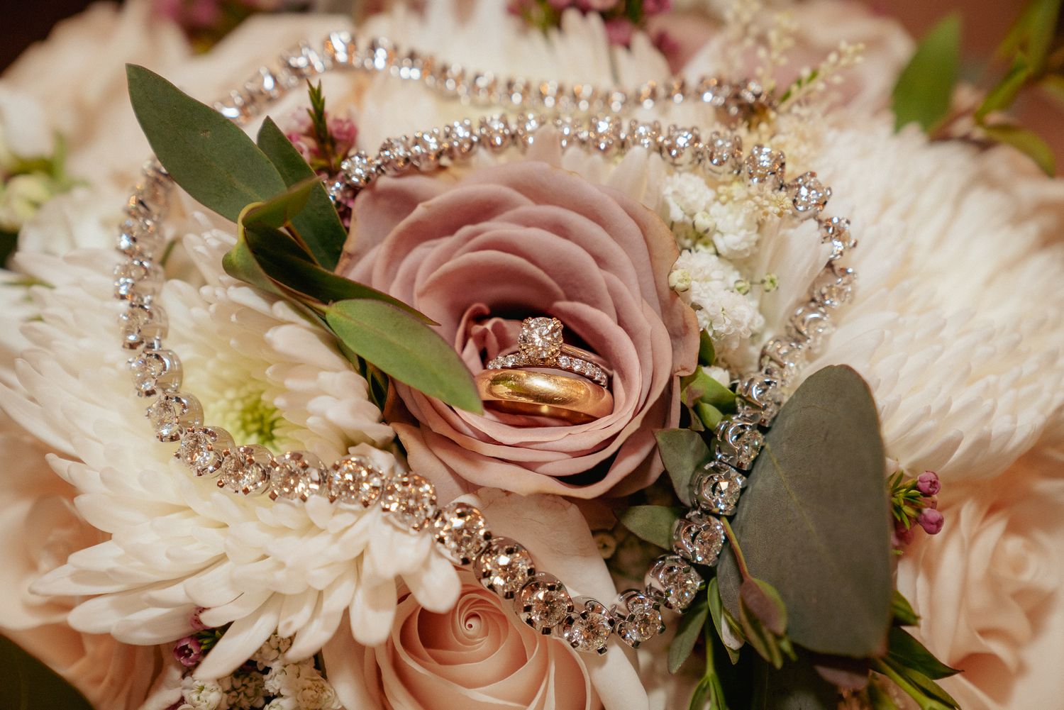 Wedding rings surrounded by soft floral bouquet and jewelry. Romantic bridal detail flat lay.