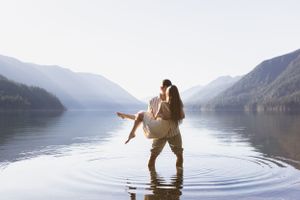 Silhouette of couple embracing in shallow lake water surrounded by mountains.